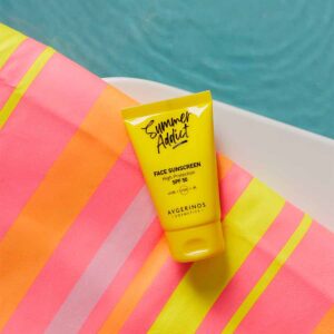 Жълта тубичка слънцезащитен крем за лице SPF 50 върху оранжево-розова раирана кърпа на ръба на басейн със синя вода
